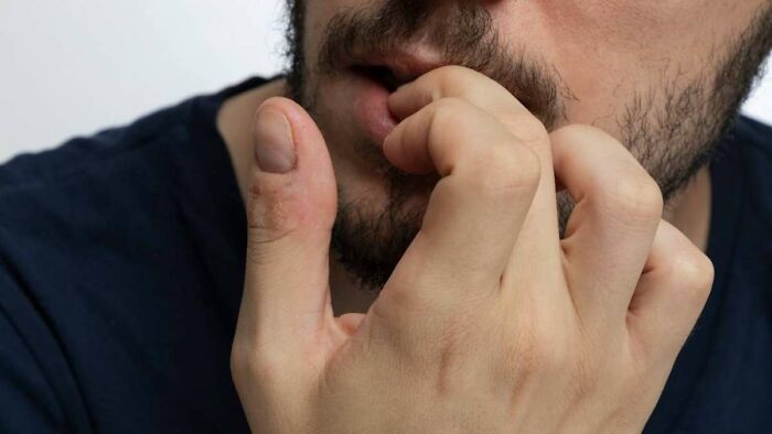 Person biting nails, showing a nervous habit; close-up on their face and hand.