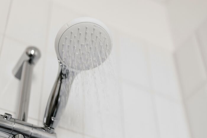 Showerhead with water flowing, silver handle; evaluating traits in daily life.