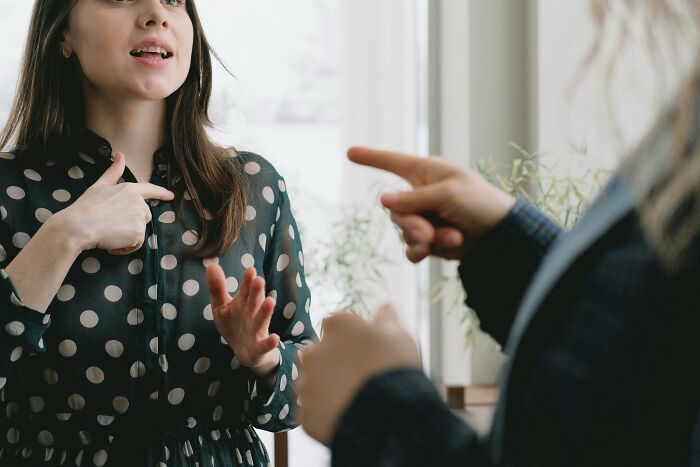 Two people in a lively discussion, using hand gestures, in a sunlit room.