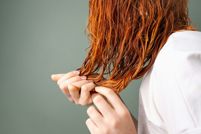Person examining their wet hair, highlighting traits and texture on a green background.
