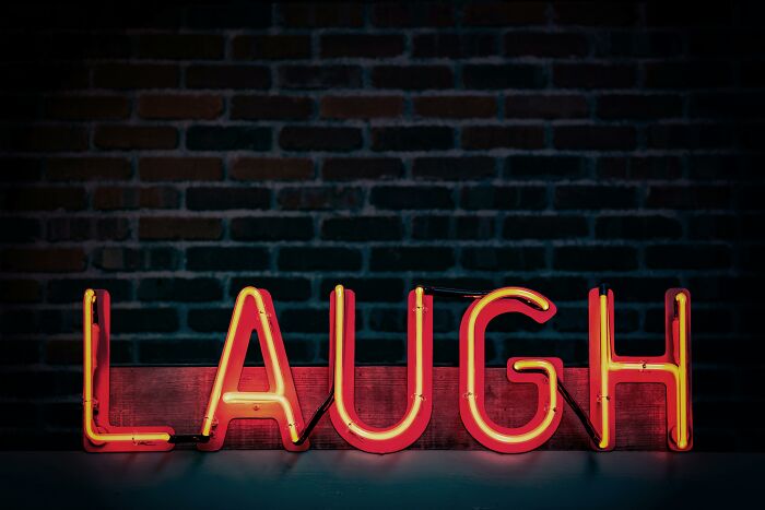 Neon sign spelling "LAUGH" against a brick wall, emphasizing opinion on humor trait.