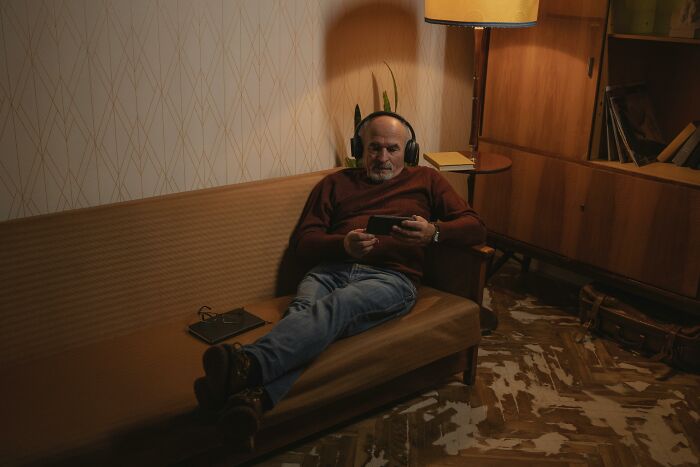 Man in headphones on a couch, using a tablet in a cozy room, reflecting on traits and rating them.
