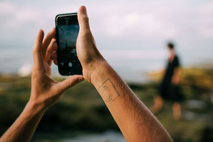 Person photographing a blurred figure with phone, focusing on opinion and traits in nature setting.