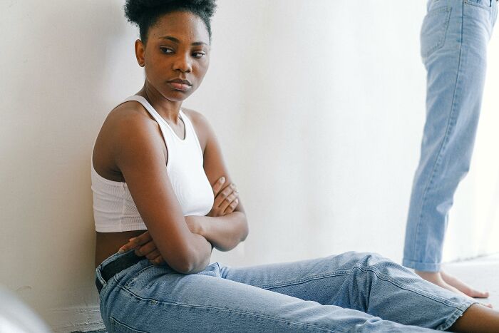 A person in casual attire with crossed arms, sitting against a wall, contemplating opinion on traits.