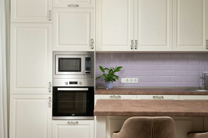 Modern kitchen with white cabinets, a built-in microwave, and a potted plant, showcasing design traits.