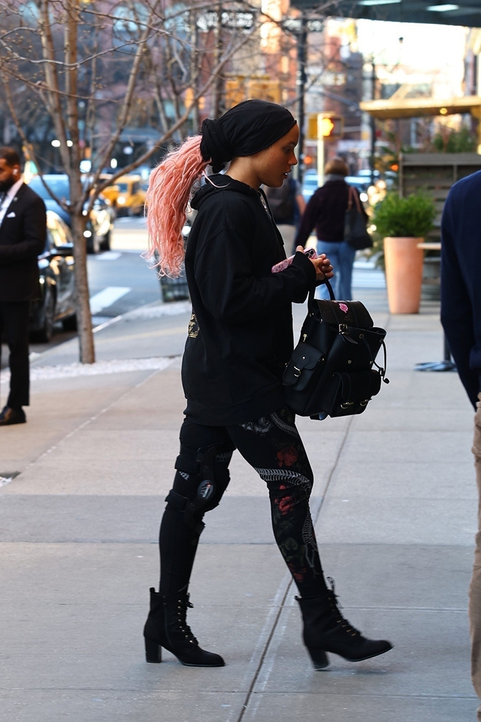 Nepo baby son walks city street in heels, pink hair, and black outfit, holding a stylish backpack. Nepo baby son walks city street in heels, pink hair, and black outfit, holding a stylish backpack.
