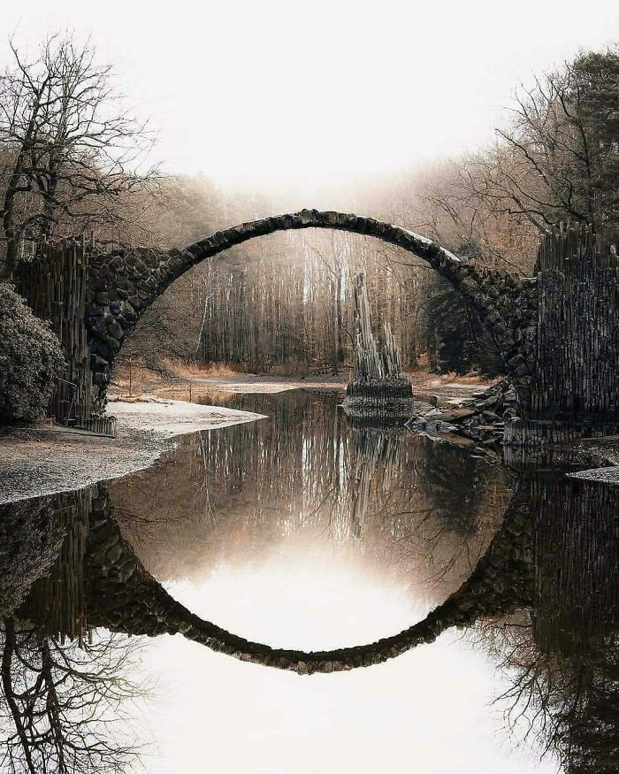 Ancient stone bridge reflected in still water, surrounded by bare trees, exemplifying the beauty of abandoned places.