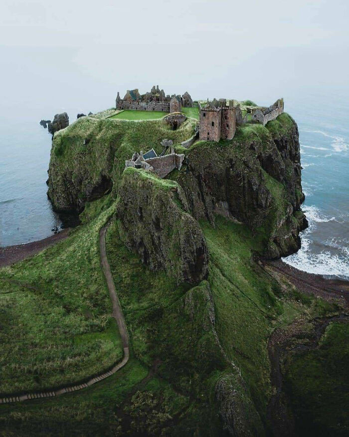 Abandoned castle on a cliff by the sea, surrounded by lush greenery and mist.