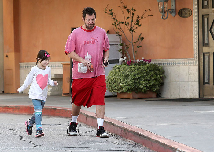 Adam Sandler in casual attire walking with a child, showcasing comedy star's relaxed lifestyle.
