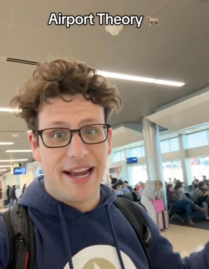 Man in an airport discussing the viral "Airport Theory" trend, wearing glasses and a blue hoodie. Man in an airport discussing the viral "Airport Theory" trend, wearing glasses and a blue hoodie.