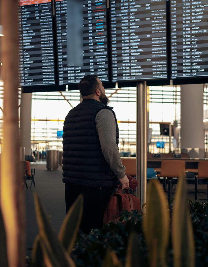 Passenger in puffer vest checking airport departure board; possibly impacted by viral airport trend. Passenger in puffer vest checking airport departure board; possibly impacted by viral airport trend.