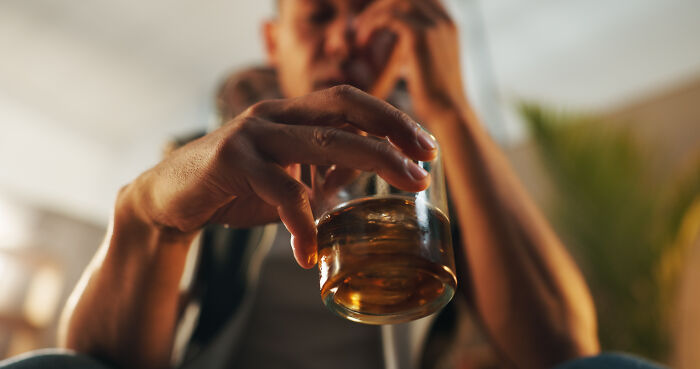 Man holding a glass of whiskey, contemplating, illustrating what type to never date again.