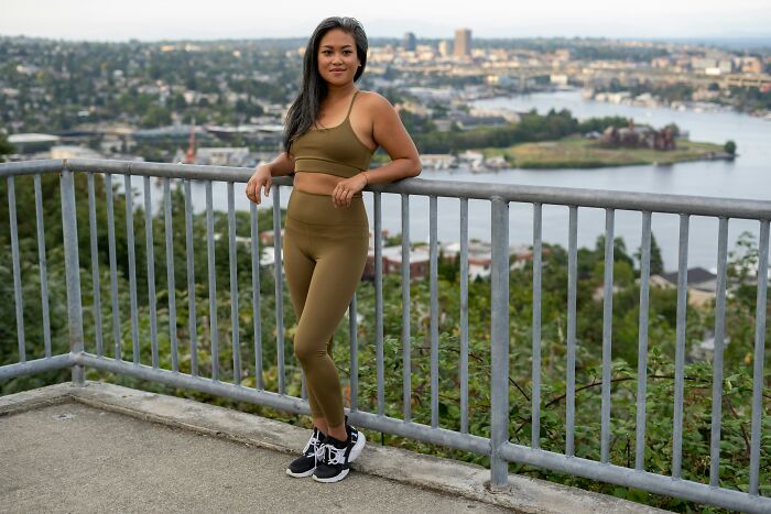 Woman in athletic wear, standing by a railing with a cityscape, showcasing unprofessional work attire in a casual setting.