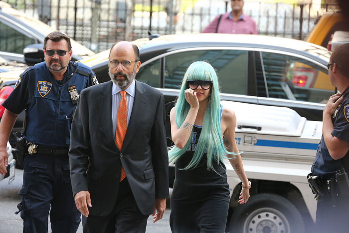Amanda Bynes with turquoise hair and sunglasses walking with two police officers.