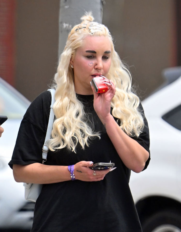 Amanda Bynes with heart tattoo under eye vaping, wearing black shirt, outdoors, reflecting a lifestyle change.
