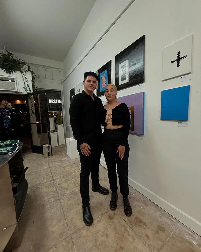 Two people, icluding Amanda Bynes, at an art gallery, standing together and wearing black outfits, exemplifying a life outside Hollywood.