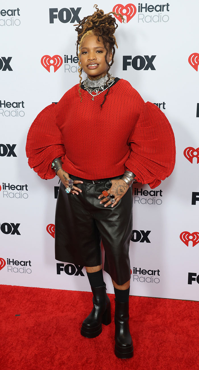 Person in bold red sweater and black shorts on red carpet at 2025 iHeartRadio Music Awards.
