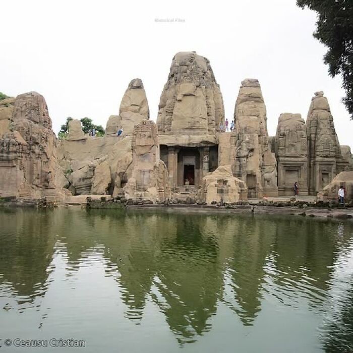 Ancient history temple reflected in a serene pond, surrounded by rocky structures and greenery.