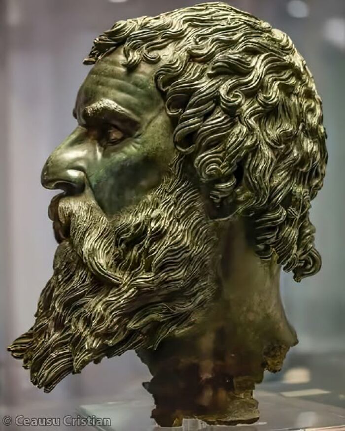 Ancient civilization bronze statue, detailed side profile with curly hair and beard.