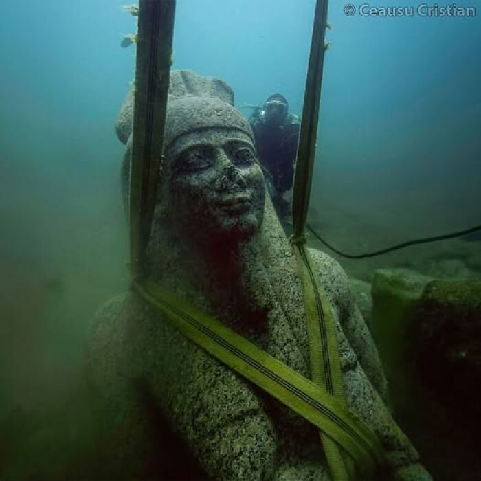 Underwater ancient statue being explored by diver, showcasing ancient history.