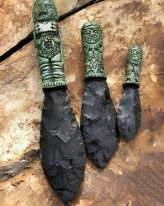 Ancient history obsidian knives with carved handles on a stone surface.