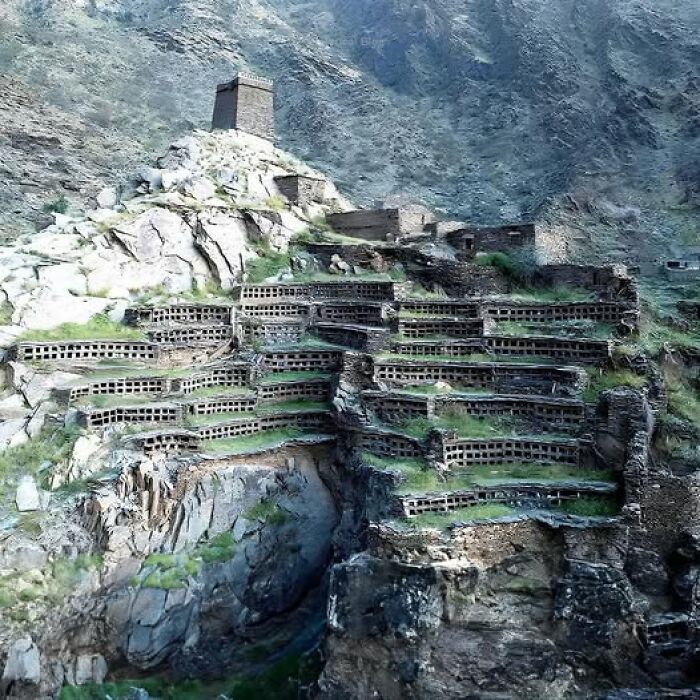 Ancient cliffside structures in rugged terrain, showcasing historical architecture thousands of years old.
