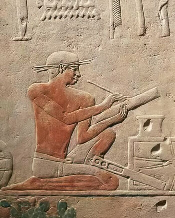 Ancient Egyptian scribe carving hieroglyphs on stone, illustrating ancient history practices.