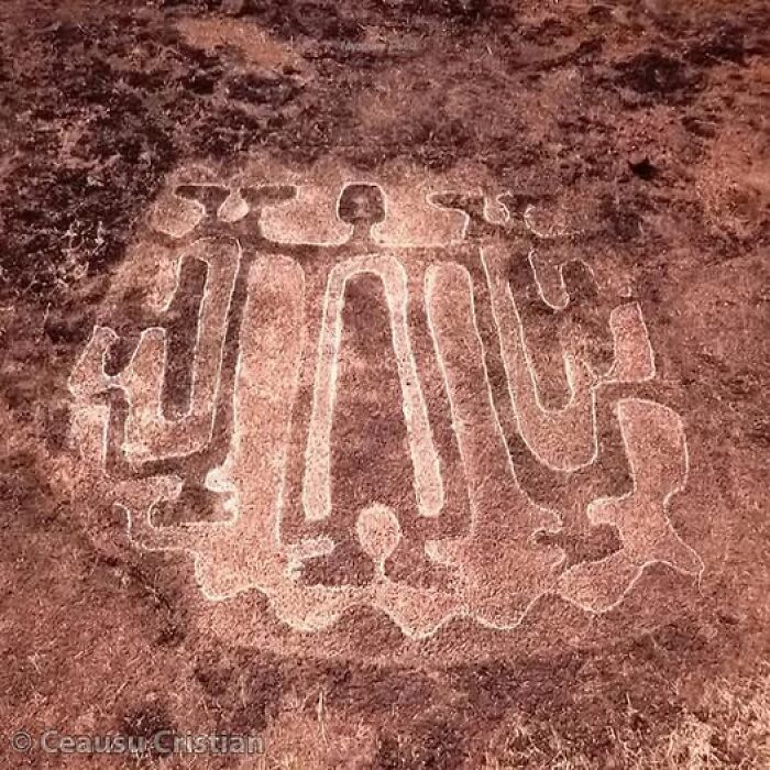 Ancient history petroglyph depicting humanoid figures etched on rocky ground.
