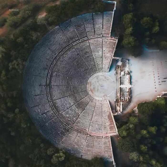Aerial view of an ancient amphitheater surrounded by trees, showcasing historical architecture.