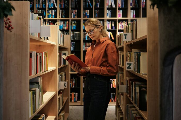 A woman in a library reads a book, surrounded by shelves, highlighting misconceptions about jobs.