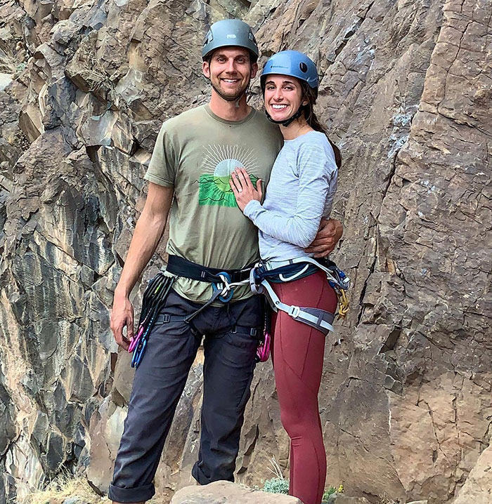 A couple with climbing gear smiling by a rock face. A couple with climbing gear smiling by a rock face.