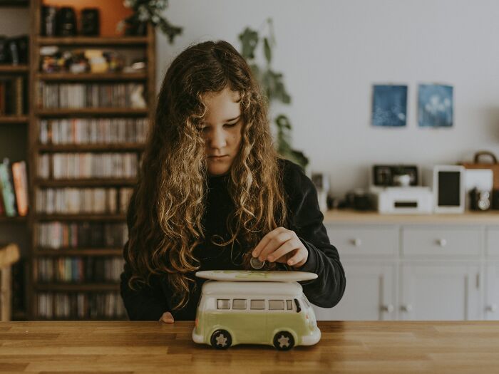 Child placing coin in a van-shaped piggy bank, illustrating an easy way to save and make money.
