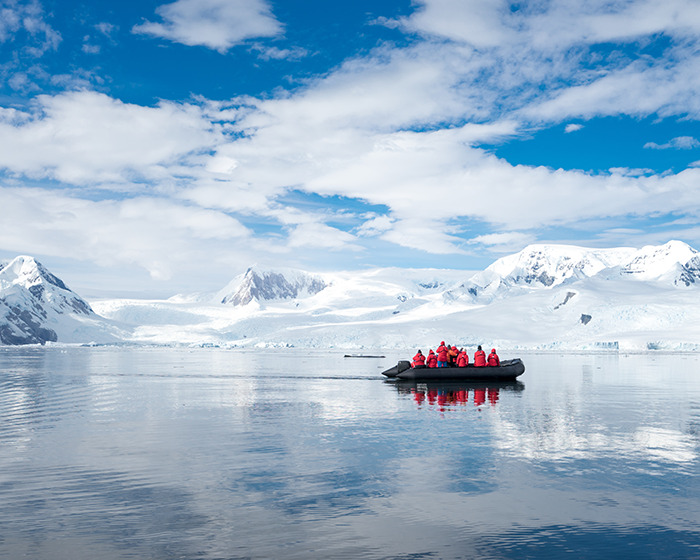 Team in red jackets exploring remote Antarctica waters in a black boat under a bright blue sky.