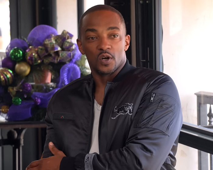 Anthony Mackie discusses masculinity, wearing a black jacket with decorative background elements.