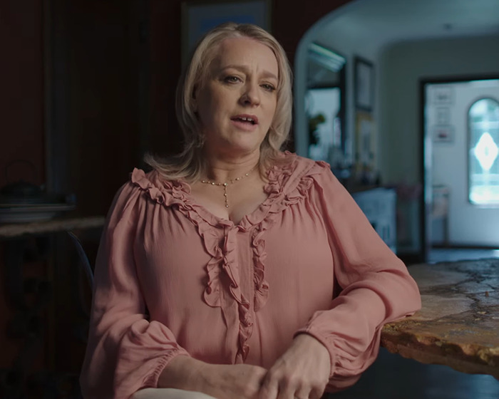 Woman in a pink blouse sitting at a table, discussing a scandal involving a disgraced actor.