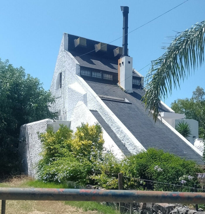 Casa de arquitectura inusual con techo inclinado y chimenea, rodeada de vegetación, destacando un posible fallo arquitectónico.