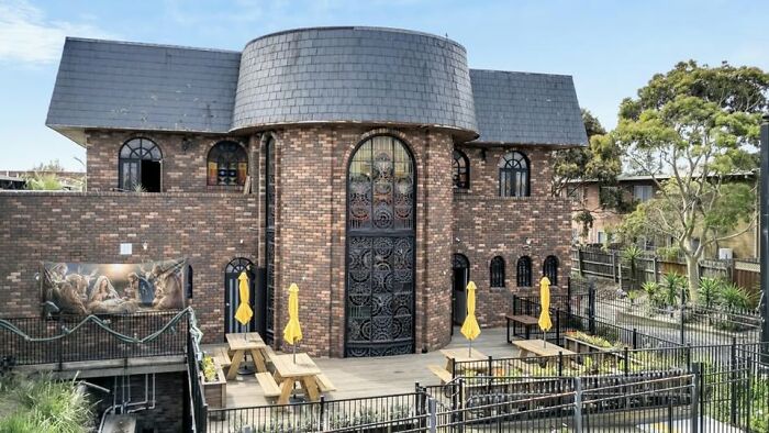 Edificio de ladrillo con diseño arquitectónico inusual, rodeado de mesas exteriores y sombrillas amarillas.