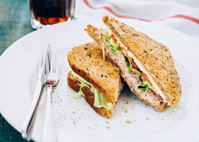 Tuna sandwich on a plate with utensils, related to workplace breakroom dining.