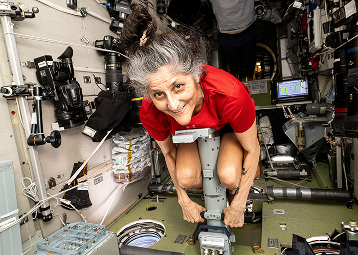 Astronaut aboard spacecraft in red shirt, demonstrating physical fitness during mission.