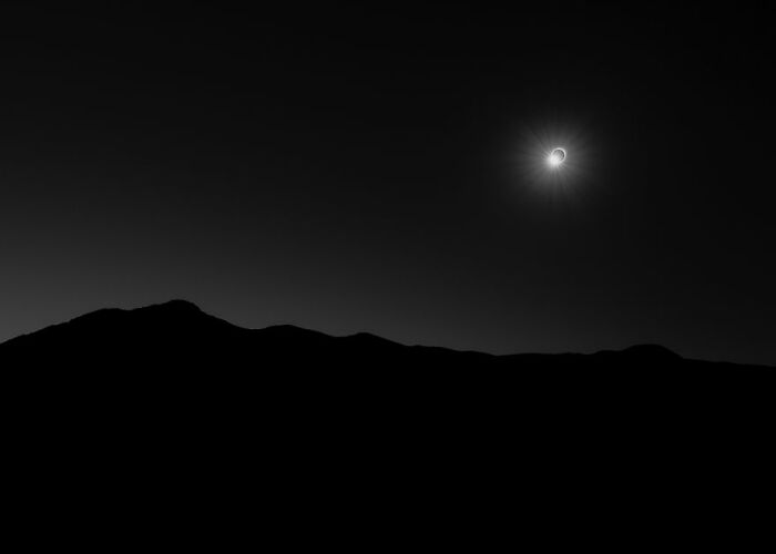 A solar eclipse over a silhouetted mountain range, capturing a stunning space phenomenon.