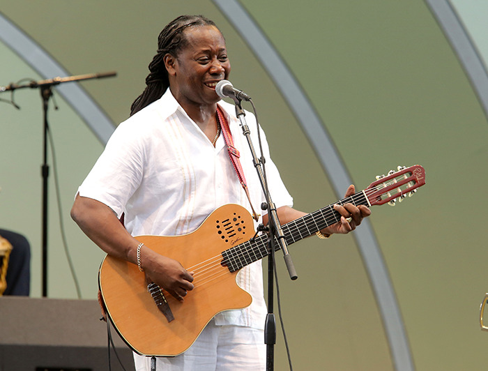 Popular singer performing with a guitar on stage in a white outfit.