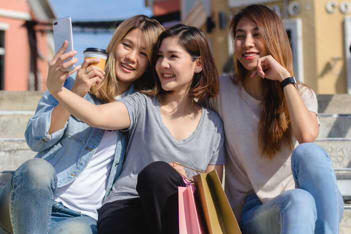 Three friends on steps taking a selfie, smiling and enjoying coffee, highlighting misunderstood social trends.