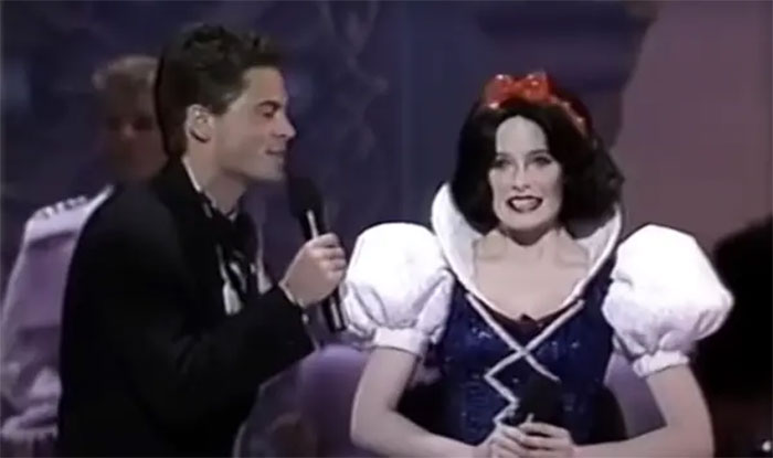 Man in tuxedo with mic and person in Snow White costume at an awards show, creating a scandalous moment.