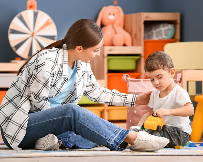 Babysitter with a child in a playroom, engaging with toys in a colorful setting.
