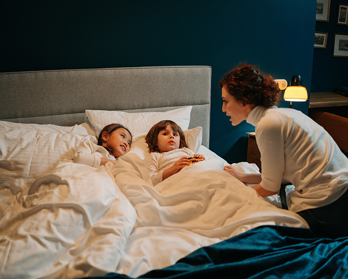Babysitter talking to two kids in bed, checking for monsters under the bed.
