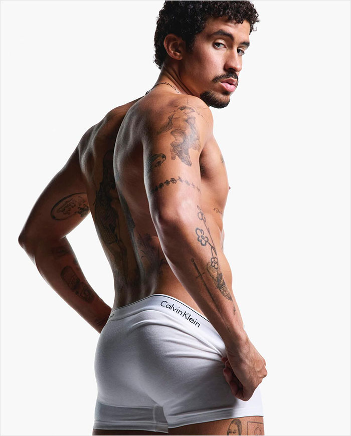 Man posing shirtless in Calvin Klein underwear, showcasing tattoos, part of viral ad campaign.