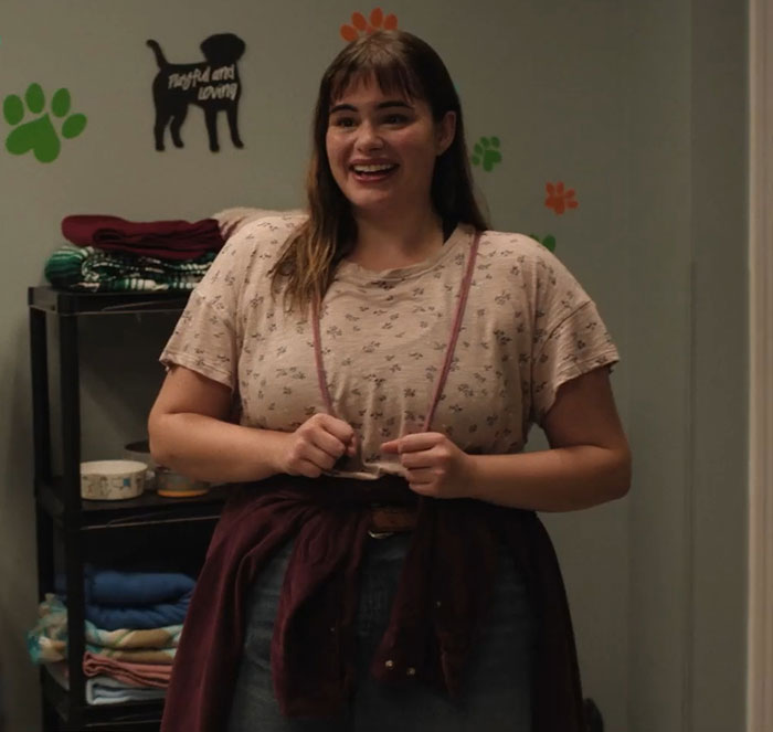 Barbie Ferreira in a movie scene before weight loss, wearing a casual outfit with dog-themed wall decor.