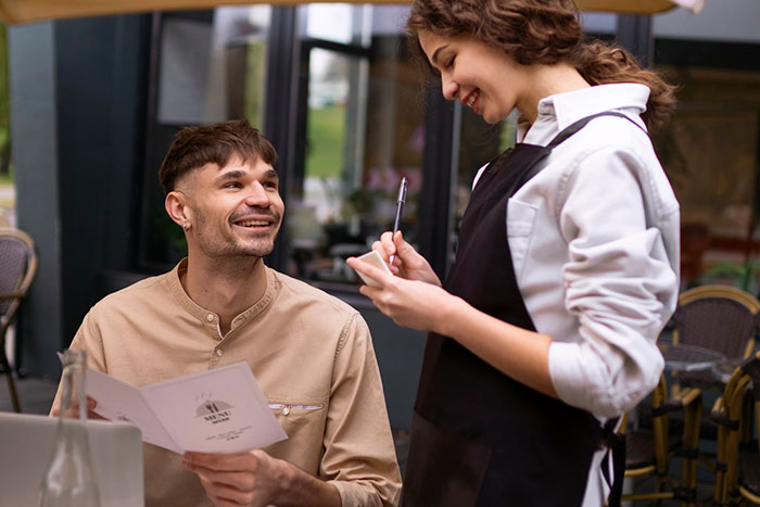 Smiling man with a menu talking to waitress, demonstrating basic knowledge in restaurant ordering.