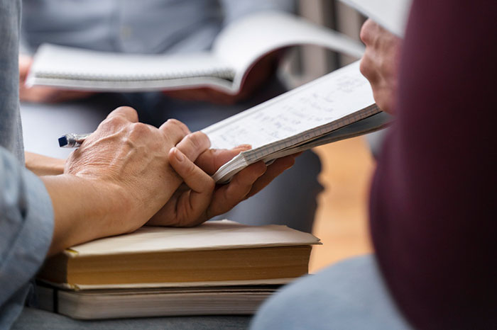 Hands exchanging basic knowledge with notebooks and pen in a study session.