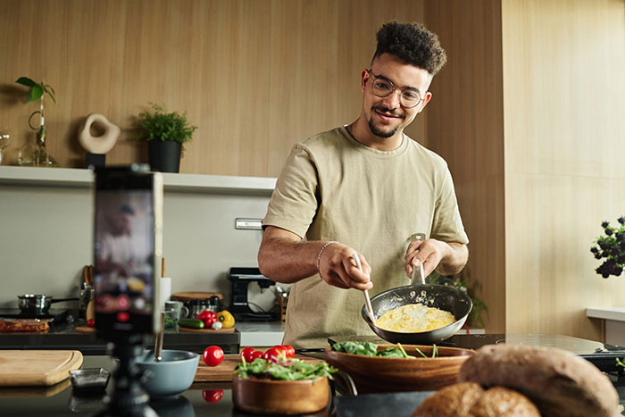 Person cooking in a kitchen, sharing basic knowledge via smartphone video.